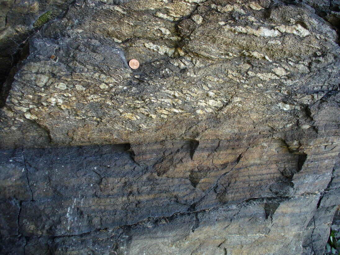 Aufschlussfoto von Gneis, im oberen Teil ist Flammengneis zu sehen, im unteren Teil ist dichter Gneis zu sehen.