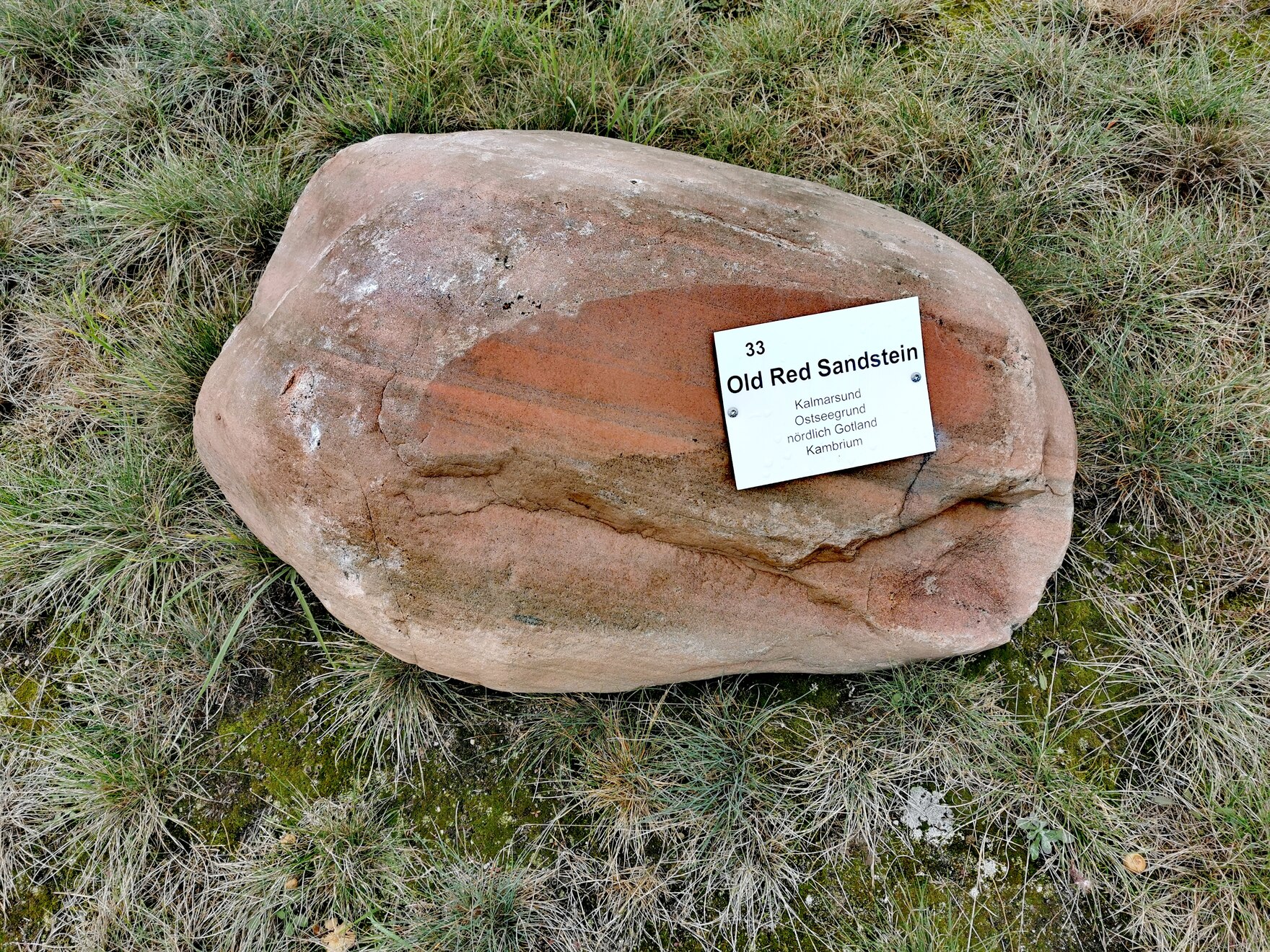 Findling aus rotem Sandstein mit Metallschild, welches seine Herkunft aus dem Kalmarsund nennt.