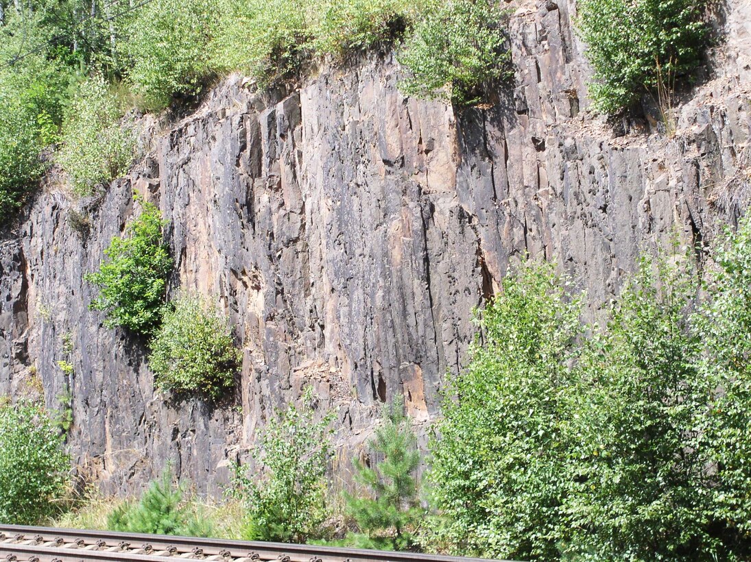 Aufschlussfoto einer Felswand am Bahneinschnitt mit vertikalen Säulen