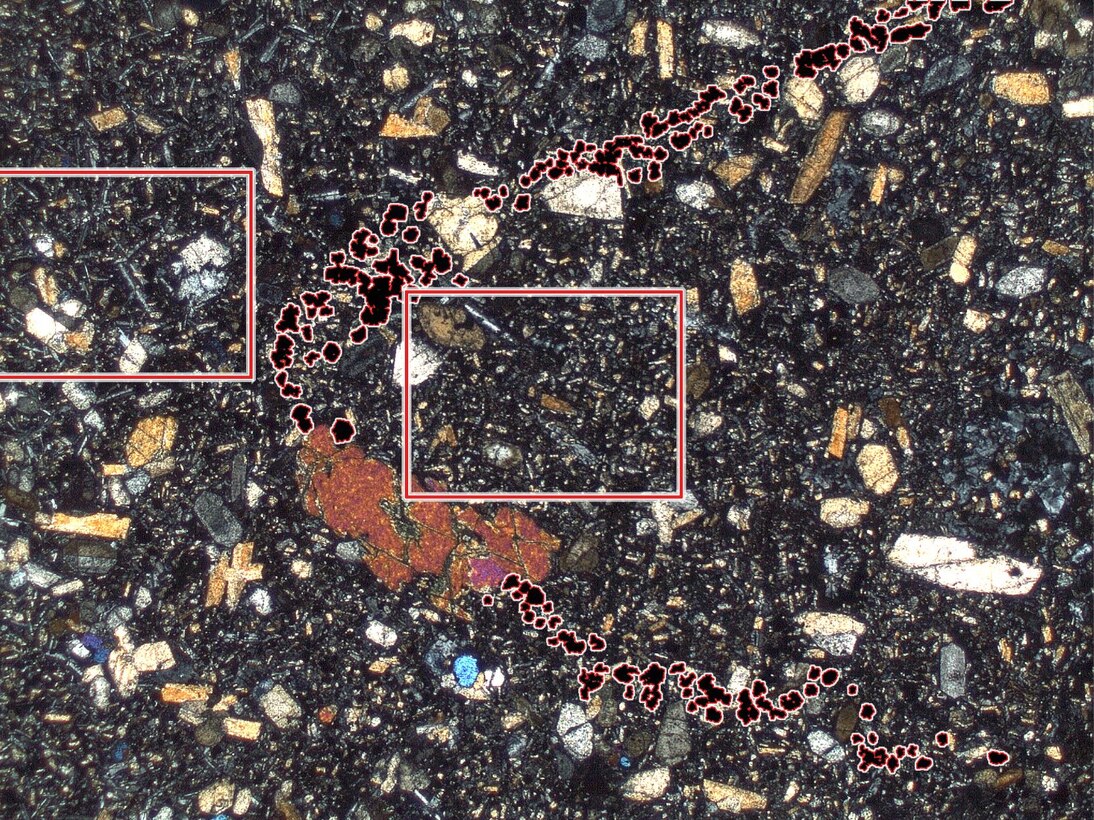 Nephelinitschliere (Zentrum und rechts) in Basanit (links, besonders oben und unten) im Dünnschliff bei Dunkelfeldmikroskopie aufgenommen. Die opaken Minerale der Kontaktzone erscheinen hier rötlich. 