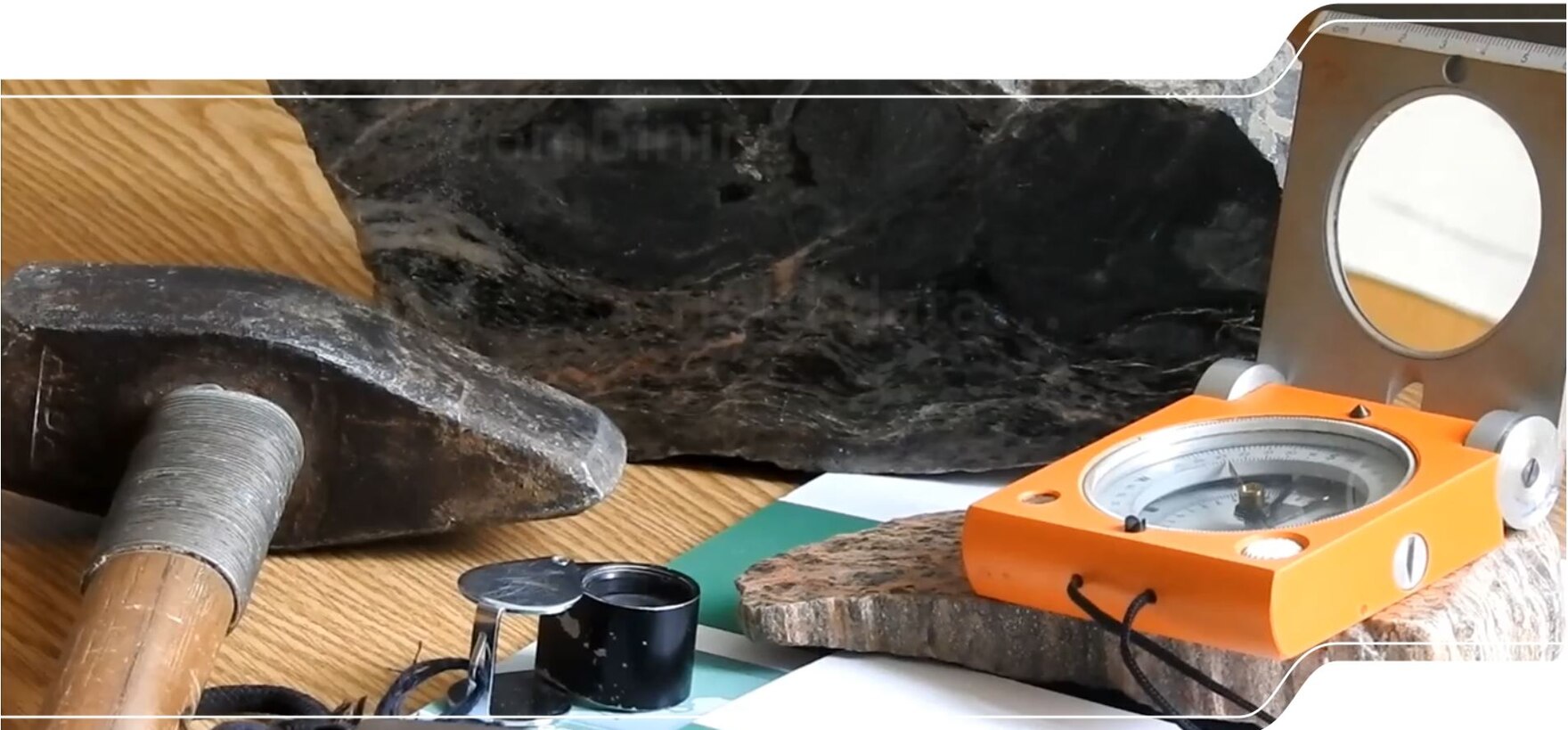 Das Bild zeigt Arbeitsgeräte des Feldgeologen: Hammer, Kompass und Lupe