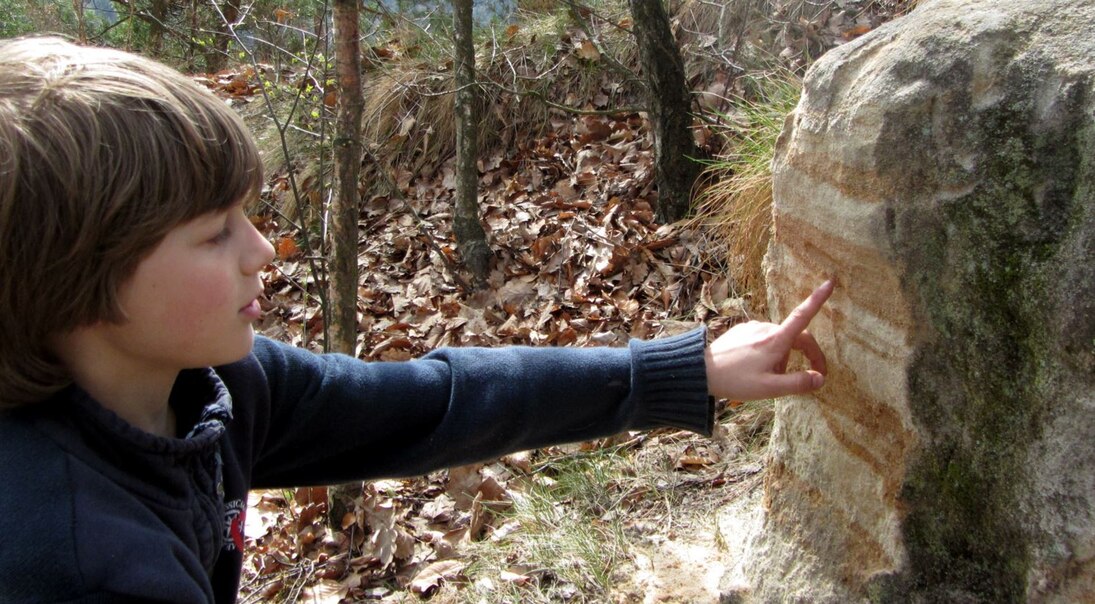 Das Bild zeigt ein Kind, welches einen Sandstein ansieht.