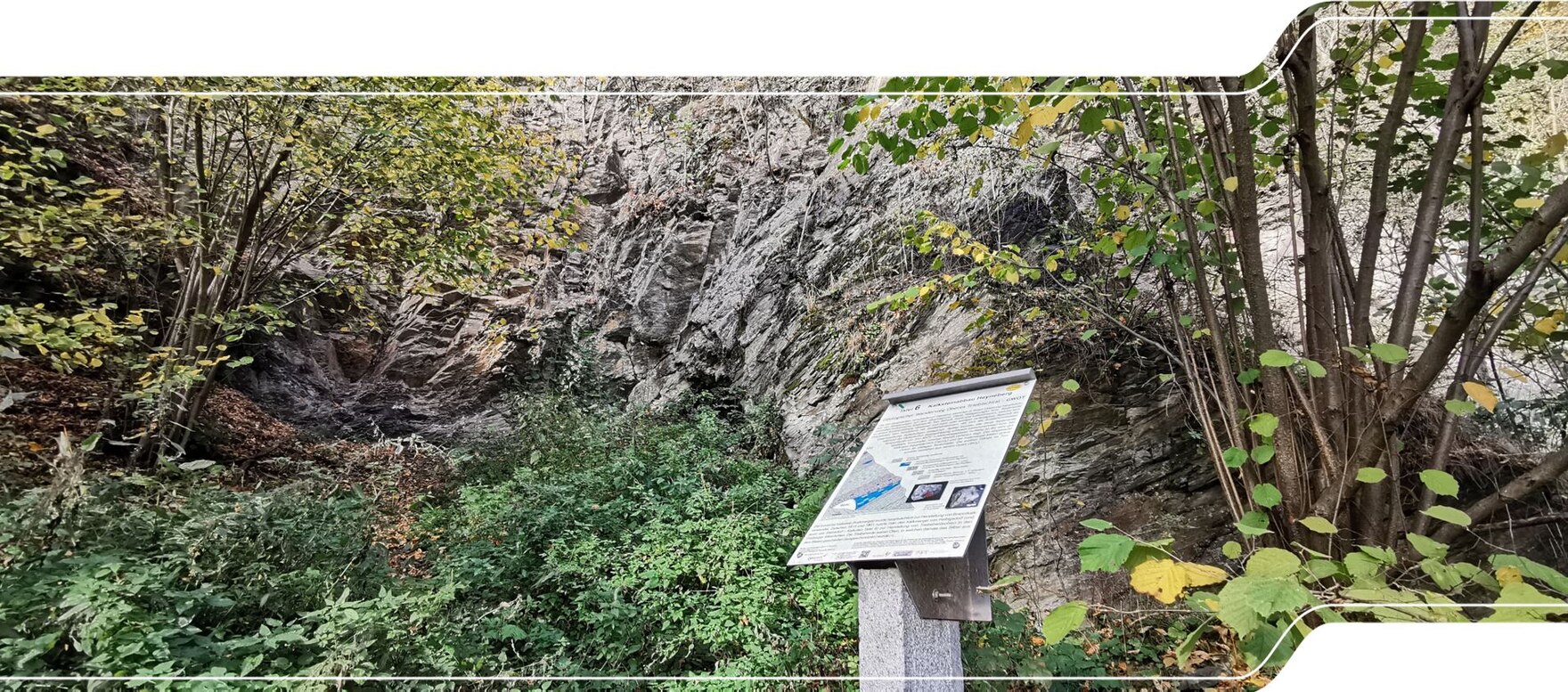 Informationstafel eines Geopfads vor einer ehemaligen Steinbruchwand.