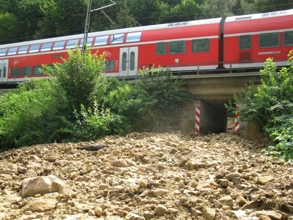 Das Bild zeigt eine eisenbahnbrücke, unter der sich ein Schlammstrom ergossen hat.