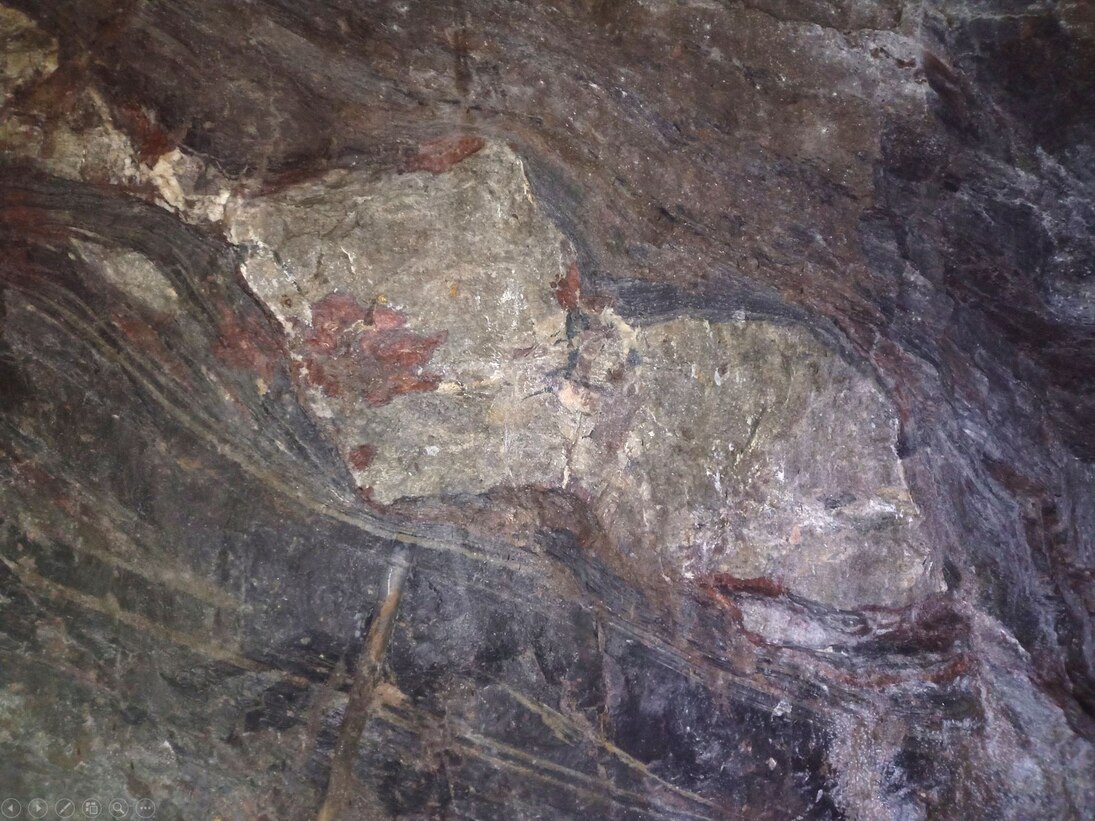 Boudin von Kalkstein in Tonstein. Boudins sind Gesteinslinsen, die entstehen, wenn spröde und duktile Gesteine gemeinsam deformiert werden. Bei der Deformation im Schiefergebirge hat der Kalkstein (Mitte, groß und hell) spröd reagiert und liegt nun als Br